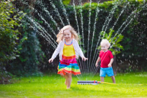 two young children running in the yard though a sprinkler