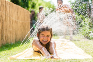 young child sliding through water sprinkler on slip and slide on sunny summer day