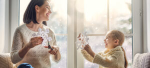 mother and daughter making snowflakes at home against snowy window