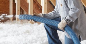 person installing white fluffy blown in insulation into attic